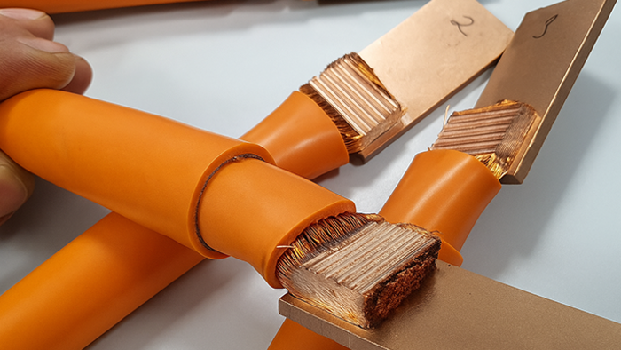 Orange-isolated copper cables with exposed stranded ends connected to flat copper busbars.